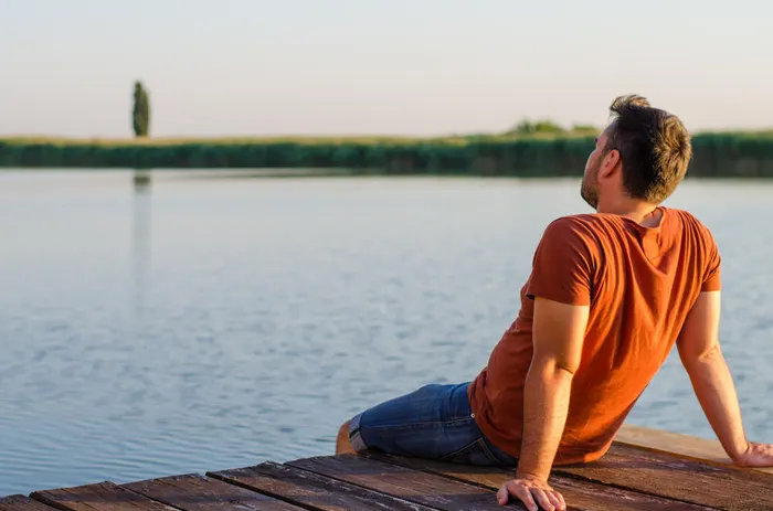Мужчина спиной к камере сидит на пирсе