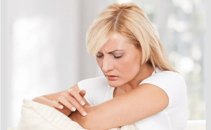 Девушка смотрит на свою руку, размышляя, на какой участок наложить трансдермальный пластырь